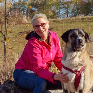 Mirjam Cordt in pinker Jacke sitzt neben einem großen Herdenschutzhund auf einer Wiese