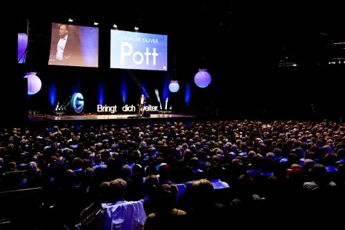 Oliver Pott spricht als Speaker auf einer großen Bühne vor vollem Saal, sein Name auf der Leinwand