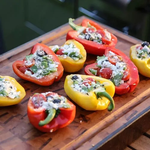 Gefüllte bunte Paprika vom Grill auf einem Holzbrett aus dem Online Grillkurs