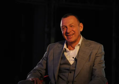 Orlando Owen im grauen Anzug sitzt lächelnd vor dunklem Hintergrund