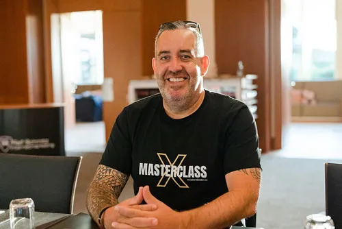 Ralf Schmitz im Masterclass-T-Shirt sitzt lächelnd an einem Tisch