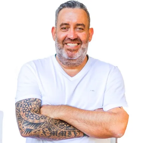 Ralf Schmitz lächelnd im weißen T-Shirt mit verschränkten, tätowierten Armen