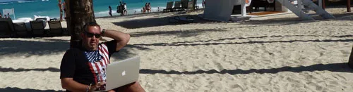Ralf Schmitz sitzt mit Laptop am Strand