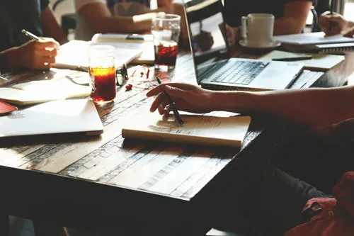 Mehrere Personen arbeiten gemeinsam an einem Holztisch mit Notizbüchern und Laptop