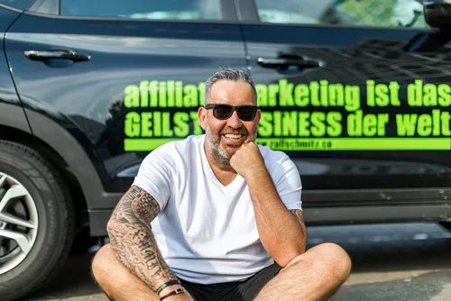 Ralf Schmitz sitzt vor einem Auto mit der Aufschrift Affiliate Marketing ist das geilste Business der Welt