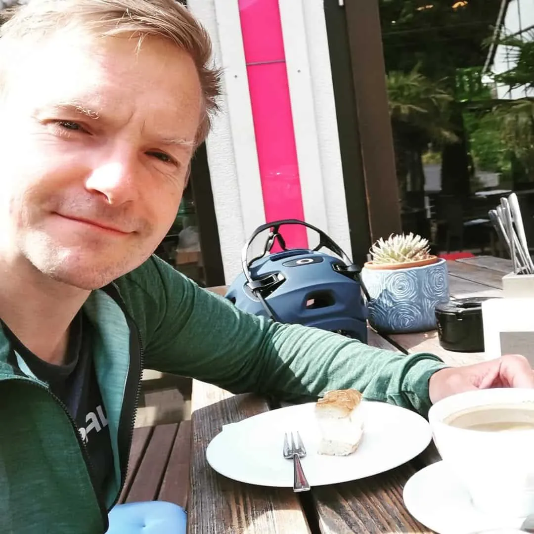 Ralf Wenda sitzt lächelnd an einem Café-Tisch mit Kaffeetasse und Kuchen