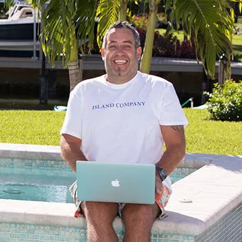 Ralf Schmitz sitzt mit Laptop am Pool vor Palmen