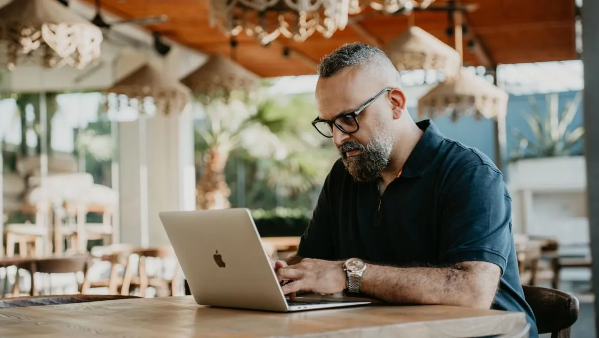 Saman Shiripour mit Brille und dunklem Poloshirt arbeitet an einem Laptop