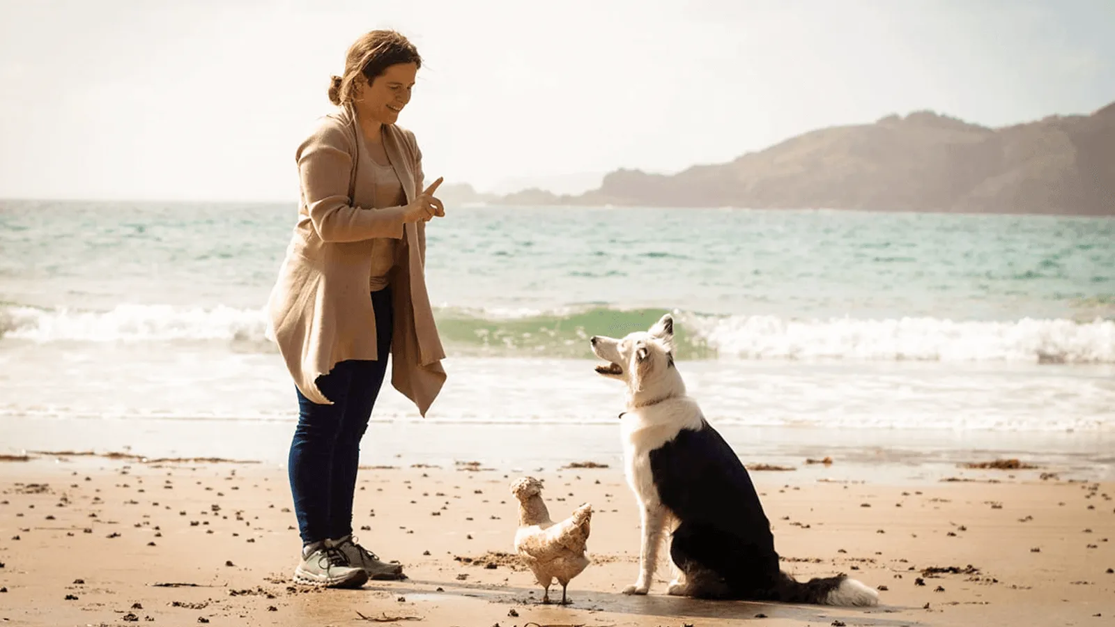 Sarah Fink am Strand gibt ihrer Border-Collie-Hündin und einem Huhn ein Handzeichen