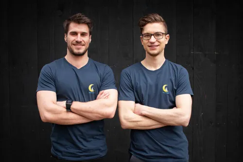 Die beiden Schlafonaut-Gründer Fabian Dittrich und Johannes Sartor mit verschränkten Armen vor dunkler Holzwand