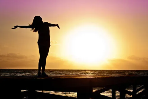 Silhouette einer Frau mit ausgebreiteten Armen vor dem Sonnenuntergang am Meer – Symbolbild für Selfmade