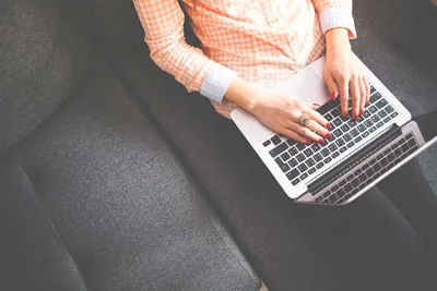Frau mit Laptop auf dem Schoß auf einem grauen Sofa – Symbolbild zum Simple Profit Kurs