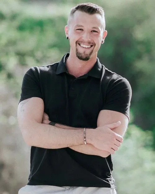 Lächelnder Stefan McLoughlin im schwarzen Poloshirt mit verschränkten Armen im Grünen