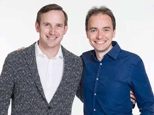 Thomas Klußmann und Christoph J. F. Schreiber lächelnd nebeneinander vor weißem Hintergrund