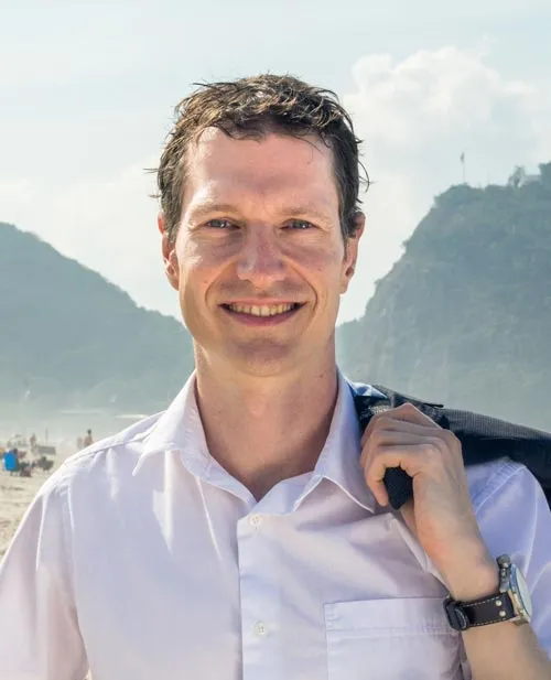 Porträt von Thorsten Wittmann im weißen Hemd vor Strand- und Berglandschaft