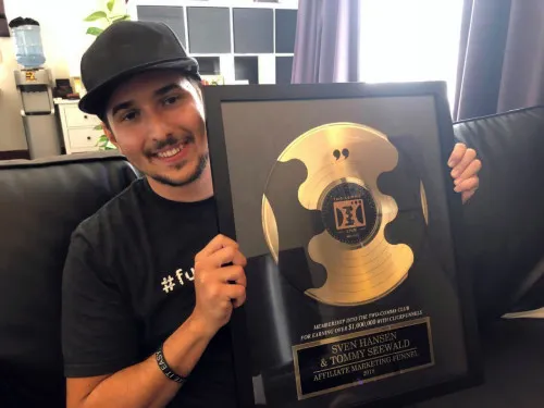 Tommy Seewald mit Basecap hält eine goldene Auszeichnung in den Händen