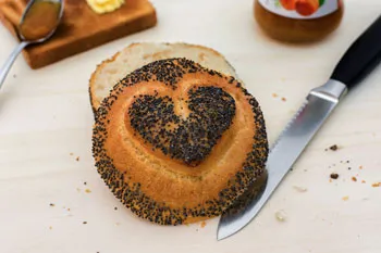 Aufgeschnittenes Mohnbrötchen mit Messer auf einem Holzbrett