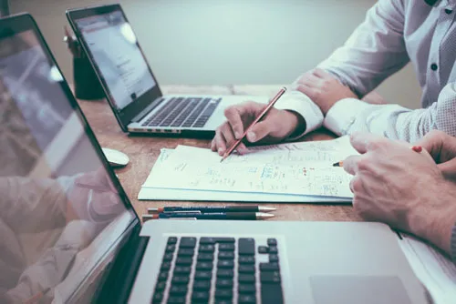 Zwei Personen arbeiten mit Laptops und Stift an Notizen auf einem Schreibtisch