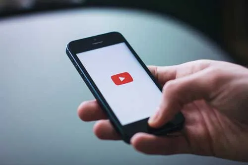 Hand hält ein Smartphone mit YouTube-Logo als Symbol für Geld verdienen mit YouTube